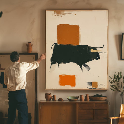 A man in a cream shirt and navy trousers stands beside a large framed abstract painting on a beige wall in a sunlit room. The painting features a cream background with a bold black bull and two orange blocks.